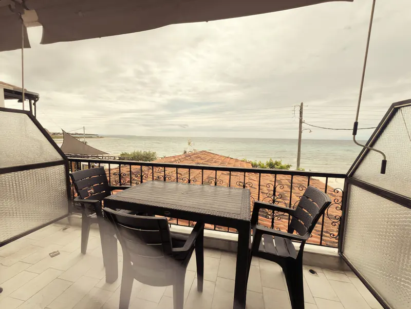 Balcony with a table and chairs above red roofs and the Thermaic Gulf