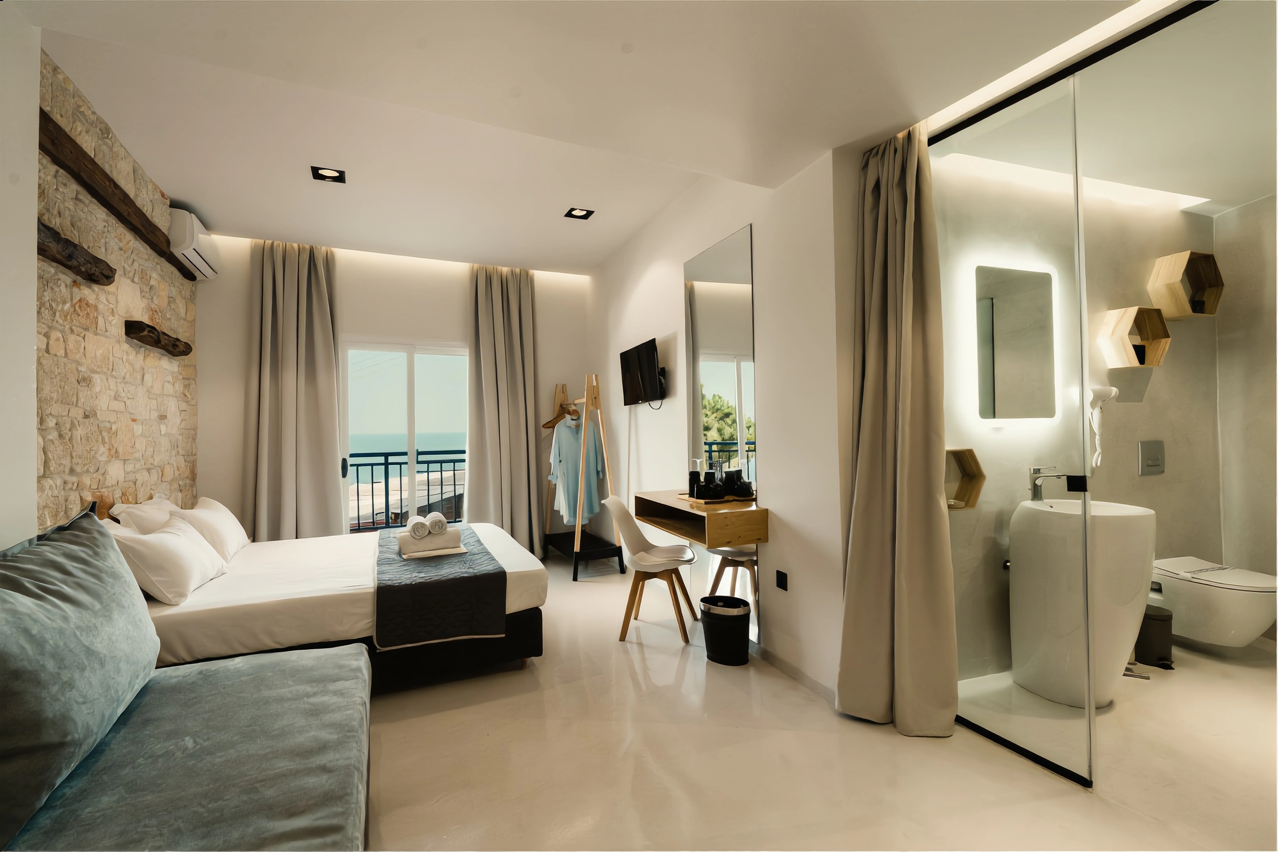 Loft with a sofa, stone wall and a glass bathroom, with the sea visible from the balcony